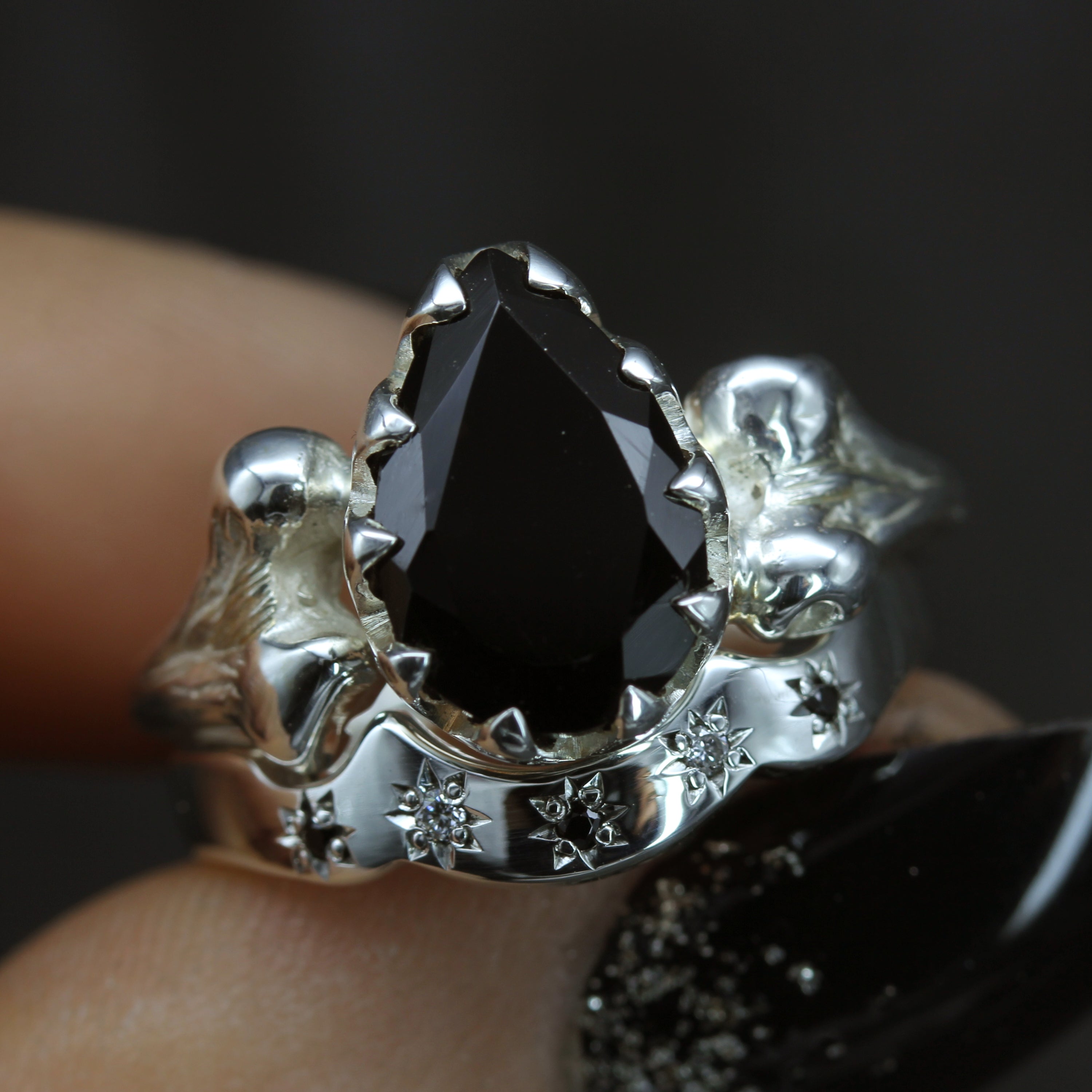 Black gemstone engagement ring with bone band, paired with wedding ring set with multiple stones.
