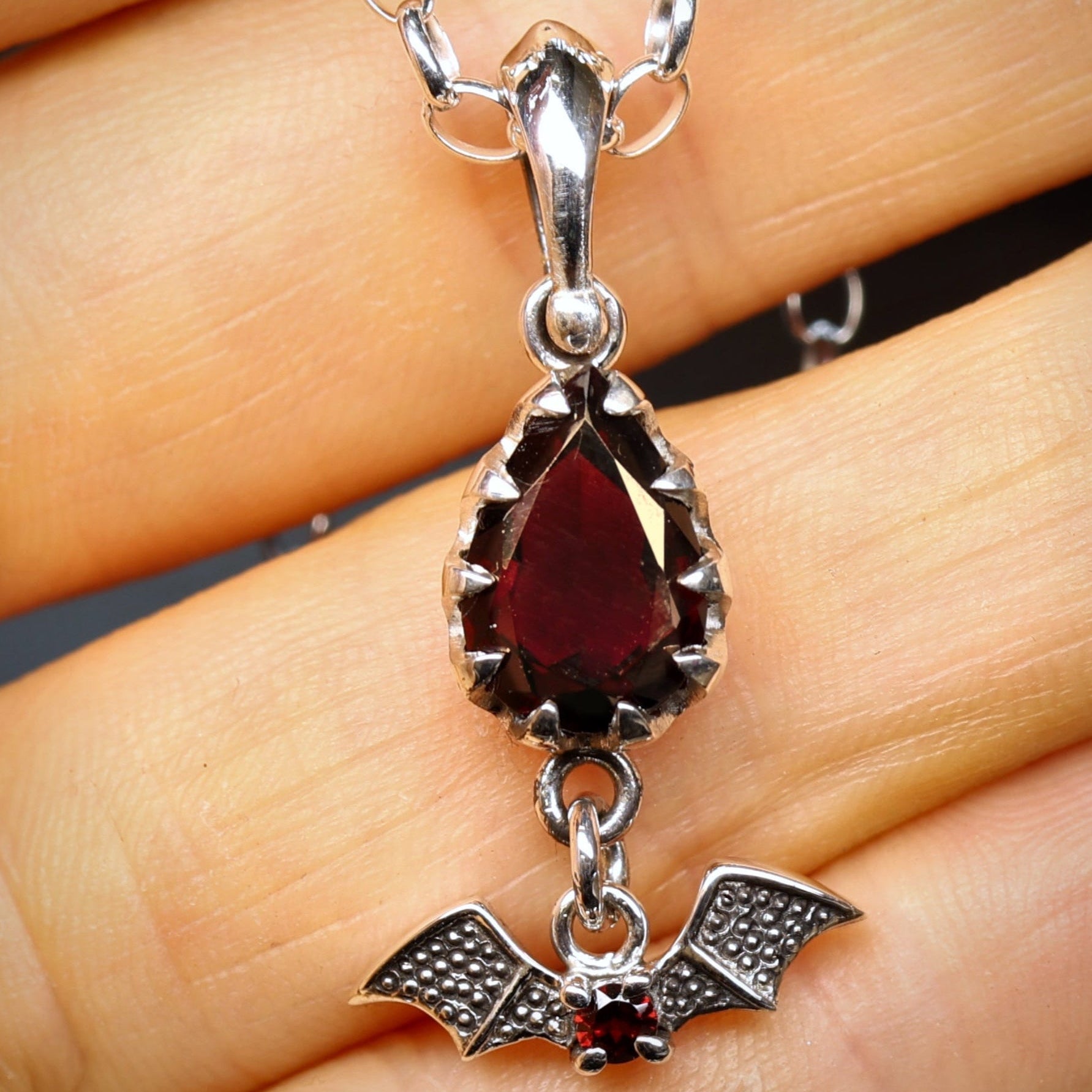 Silver necklace with a red gemstone pendant held in hand
