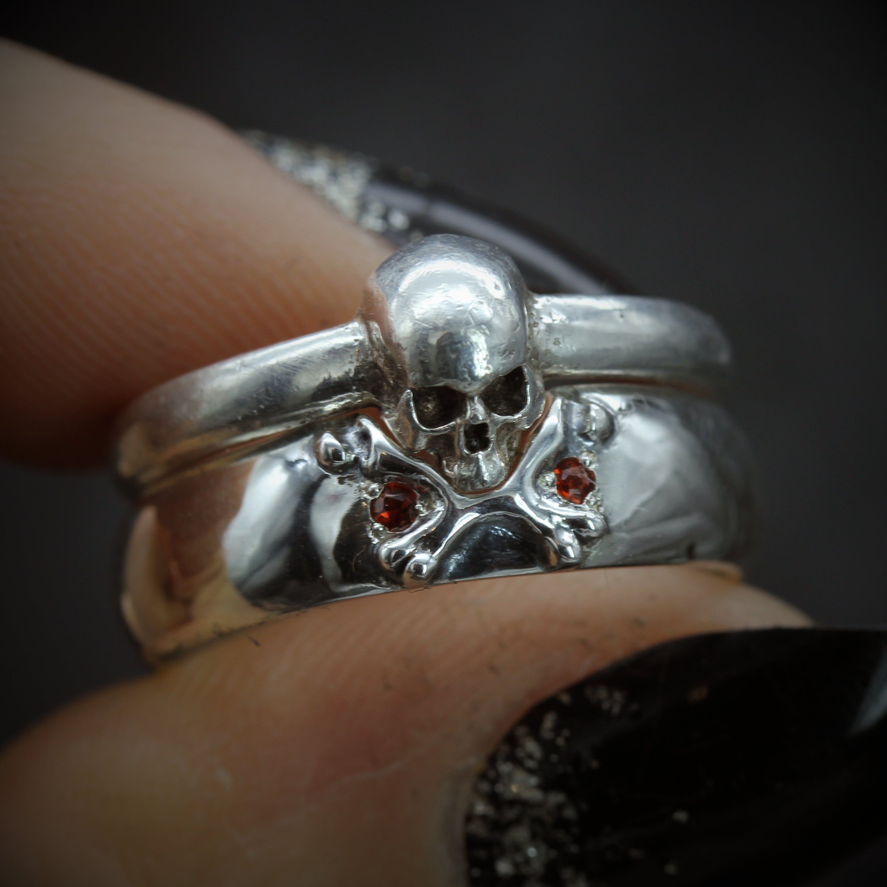 Skull ring paired with cross bone ring, held in fingers