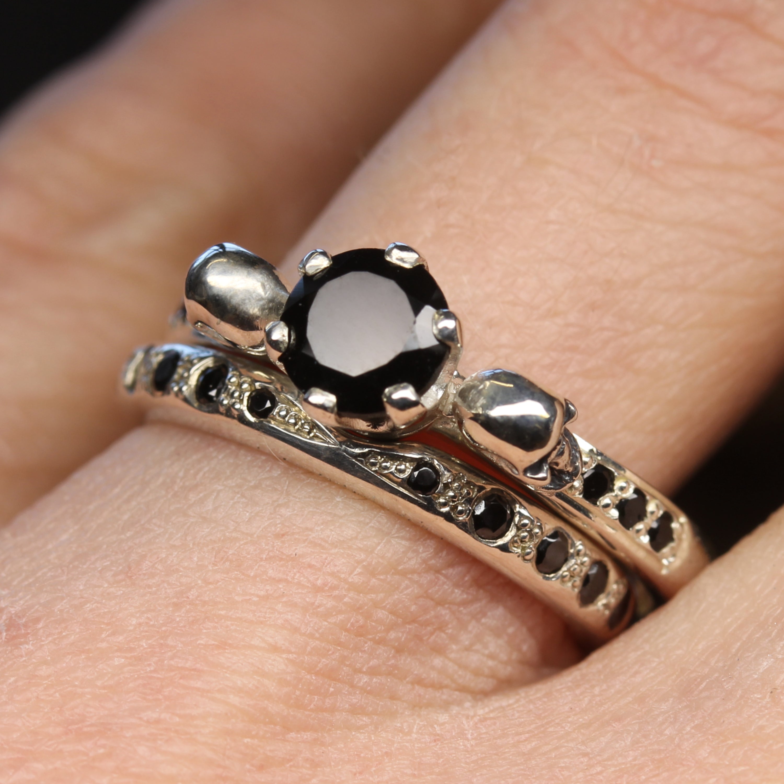 Women's Silver Skull Wedding Ring with Black Spinel next to Silver Skull Engagement Ring, on finger.