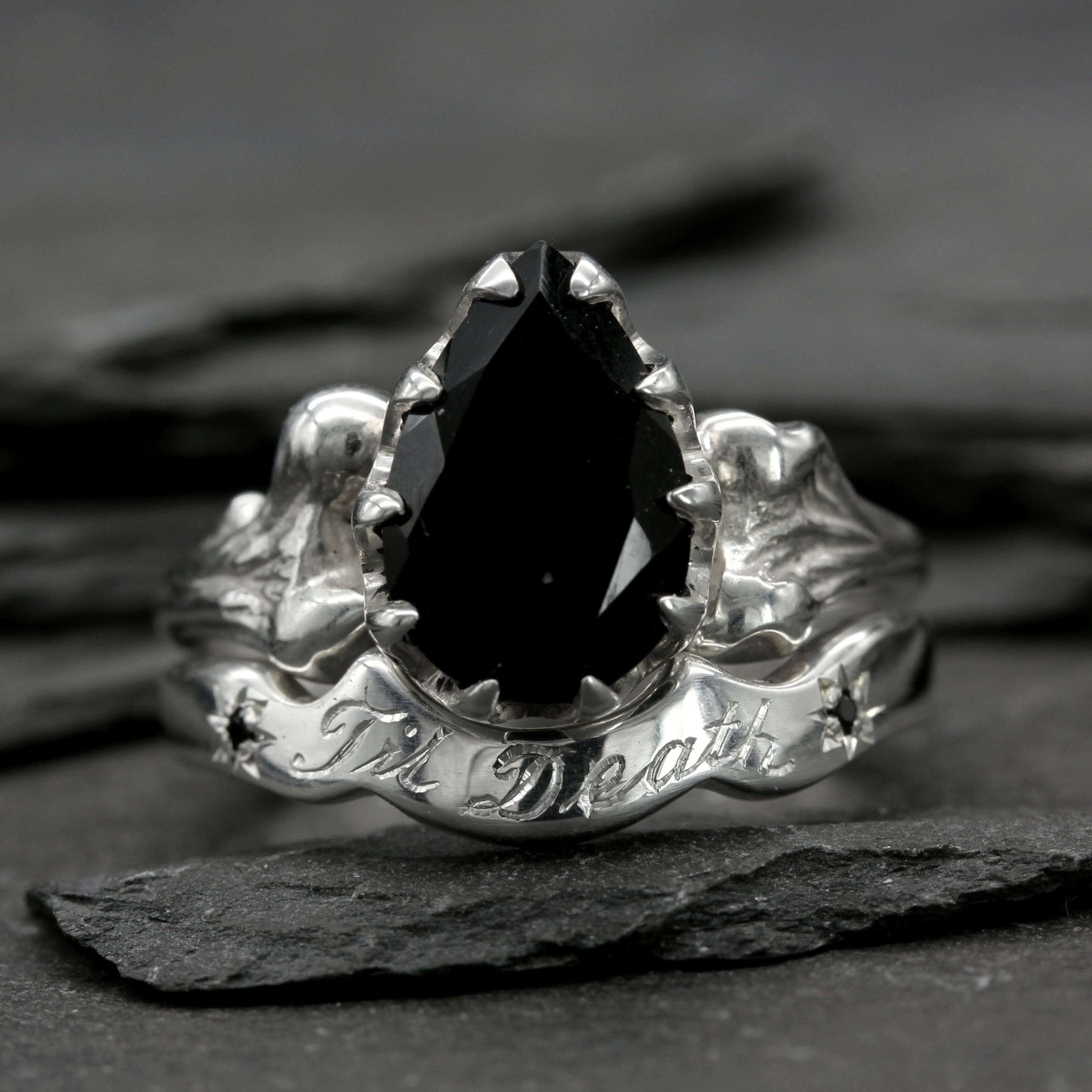 Til Death Wedding Ring paired with Bone Engagement ring, set with black gemstone. On table.