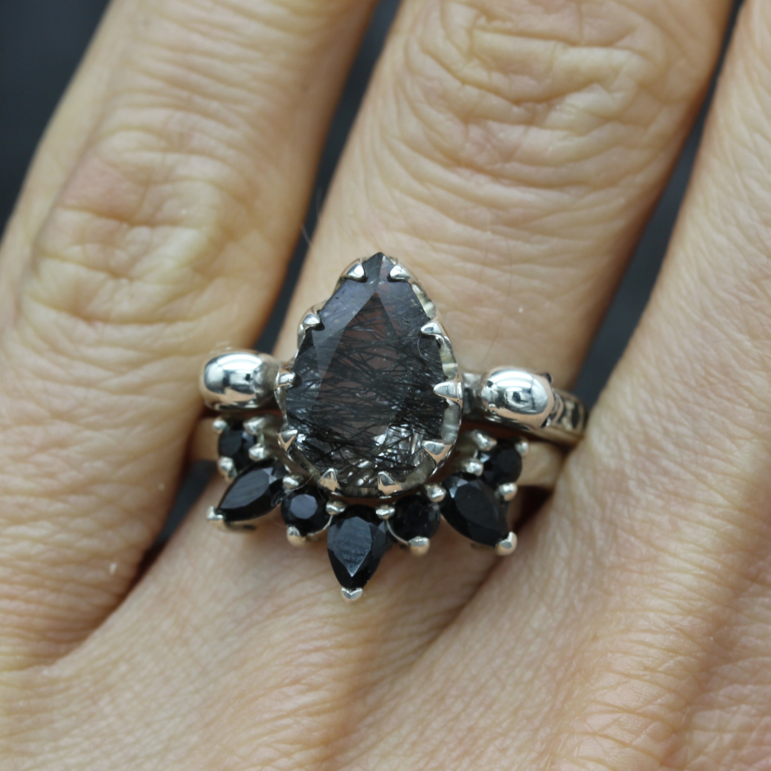 Pear Cut Tourmalated Quartz Skull Engagement ring with gothic wedding ring below, on finger.