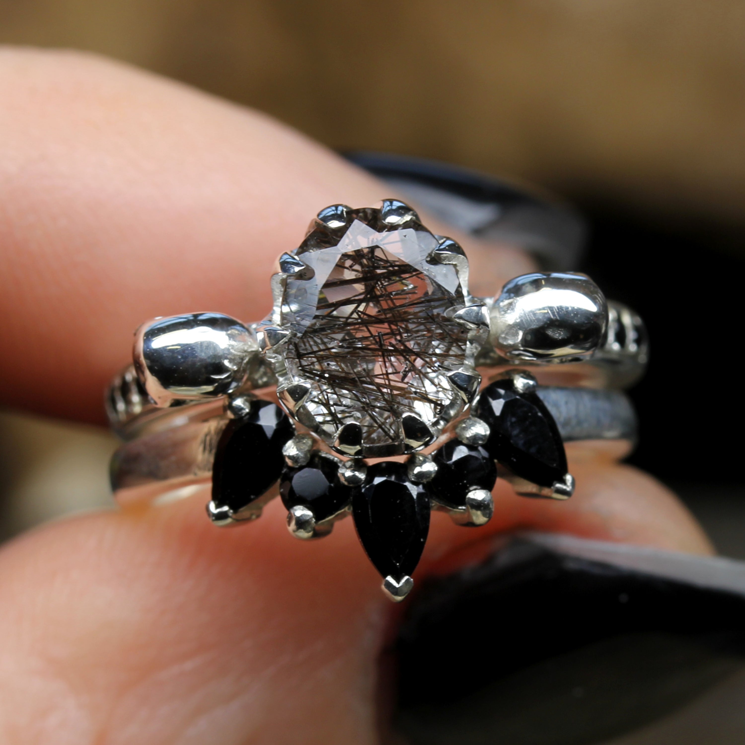 Oval Tourmalated Quartz Skull Engagement Ring with Black Gemstone Crown. Held between Fingers.