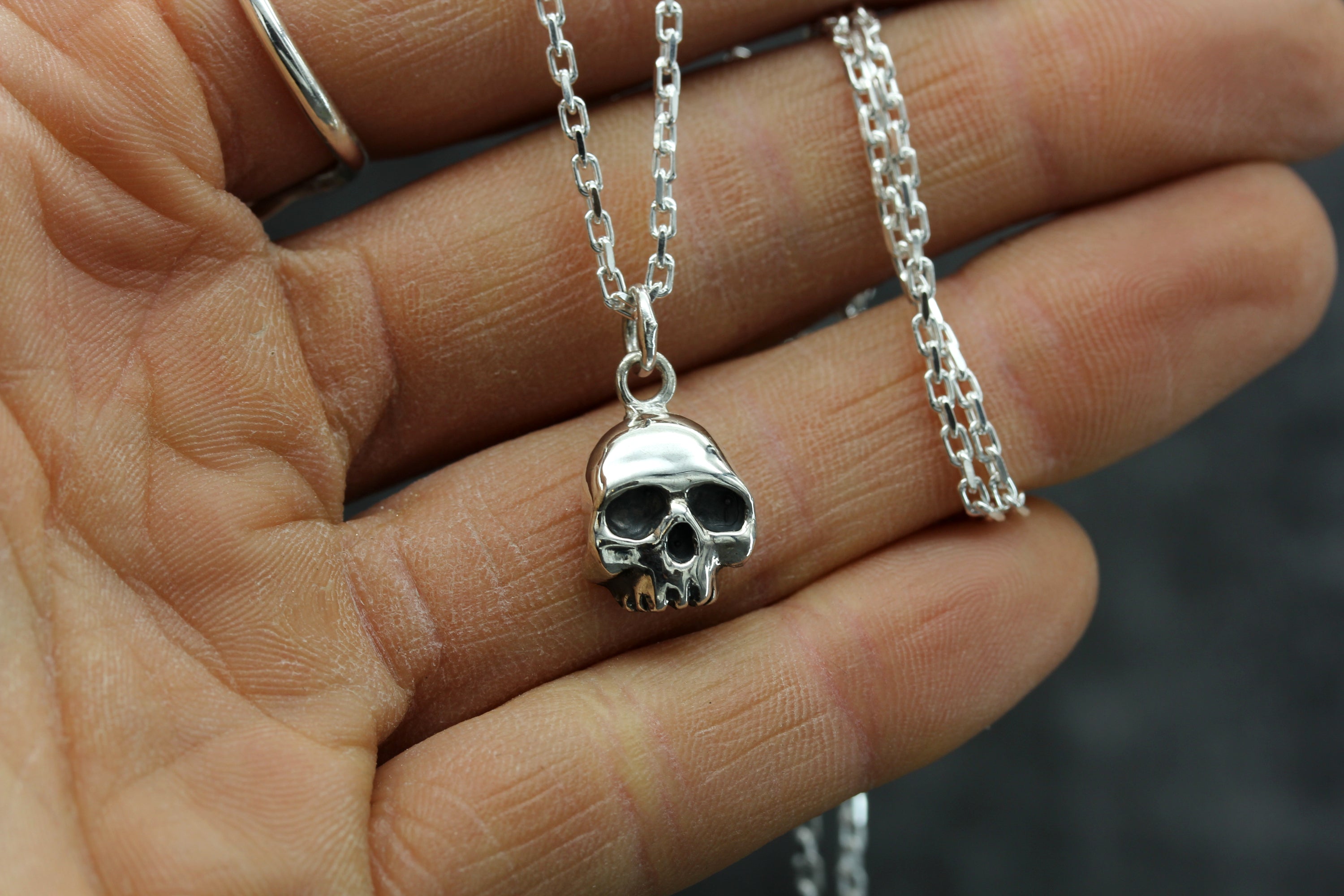 Silver Skull Necklace being held against the palm of a hand