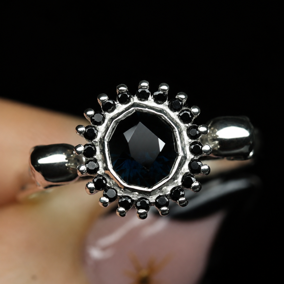 9ct white gold skull engagement ring with a faceted dark blue black sapphire centre stone, surrounded by a halo of black spinel gemstones