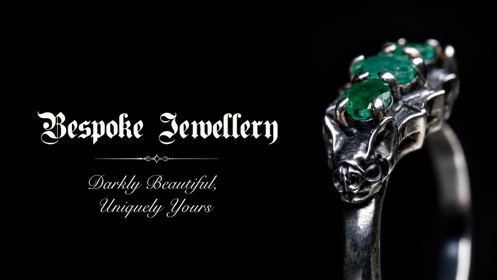 Silver bat gothic engagement ring with emeralds on a black background, featuring the brand 'Bespoke Jewellery'.
