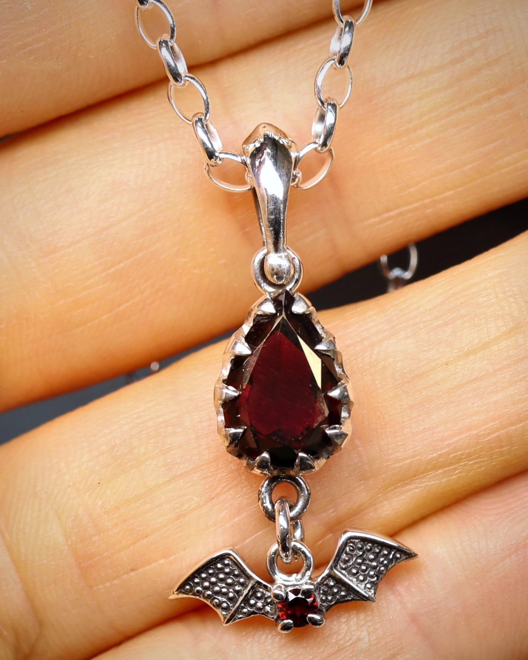 Silver necklace with a red gemstone pendant held in hand